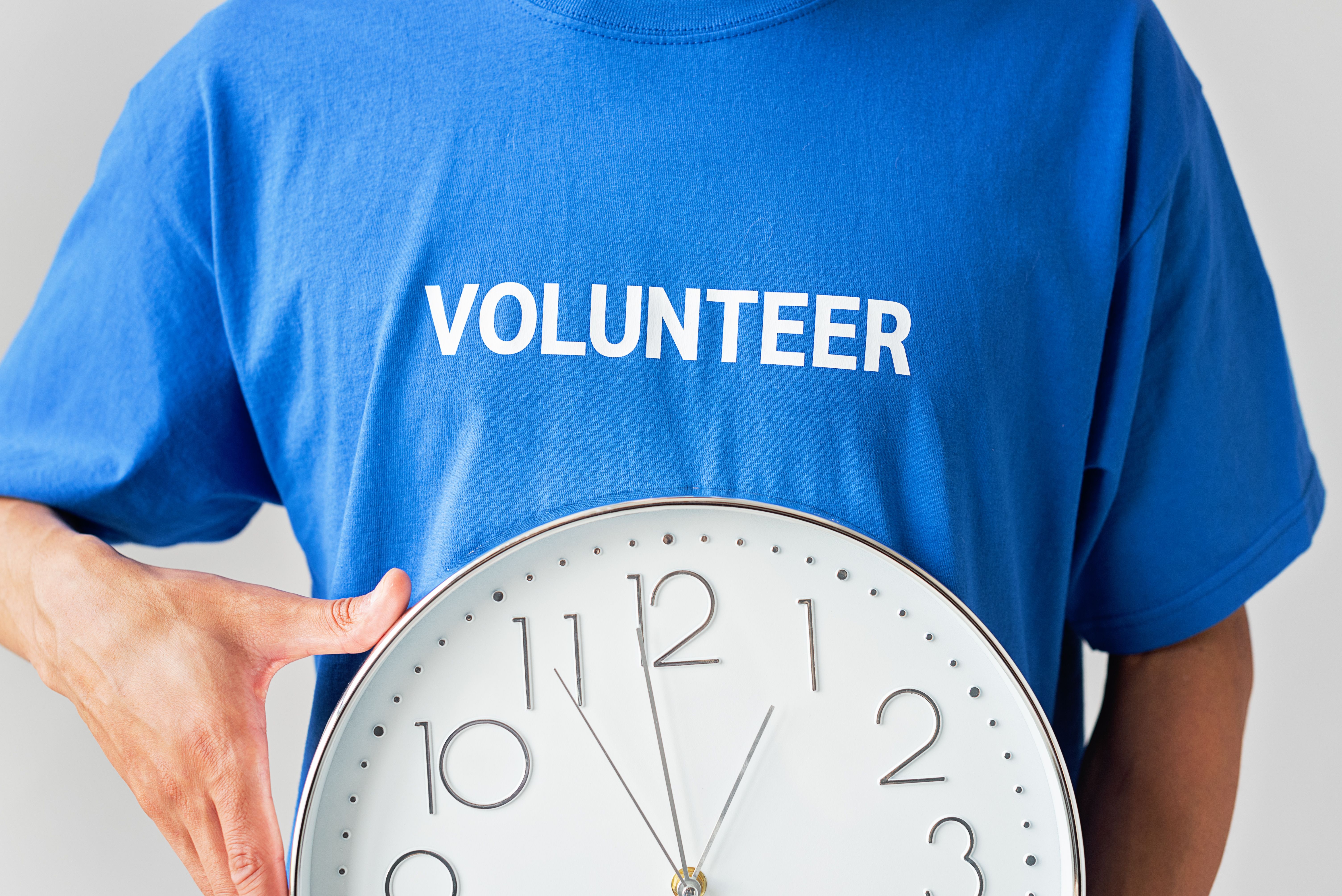 Bénévole portant un t-shirt « Volunteer » et tenant une horloge, symbole du temps donné